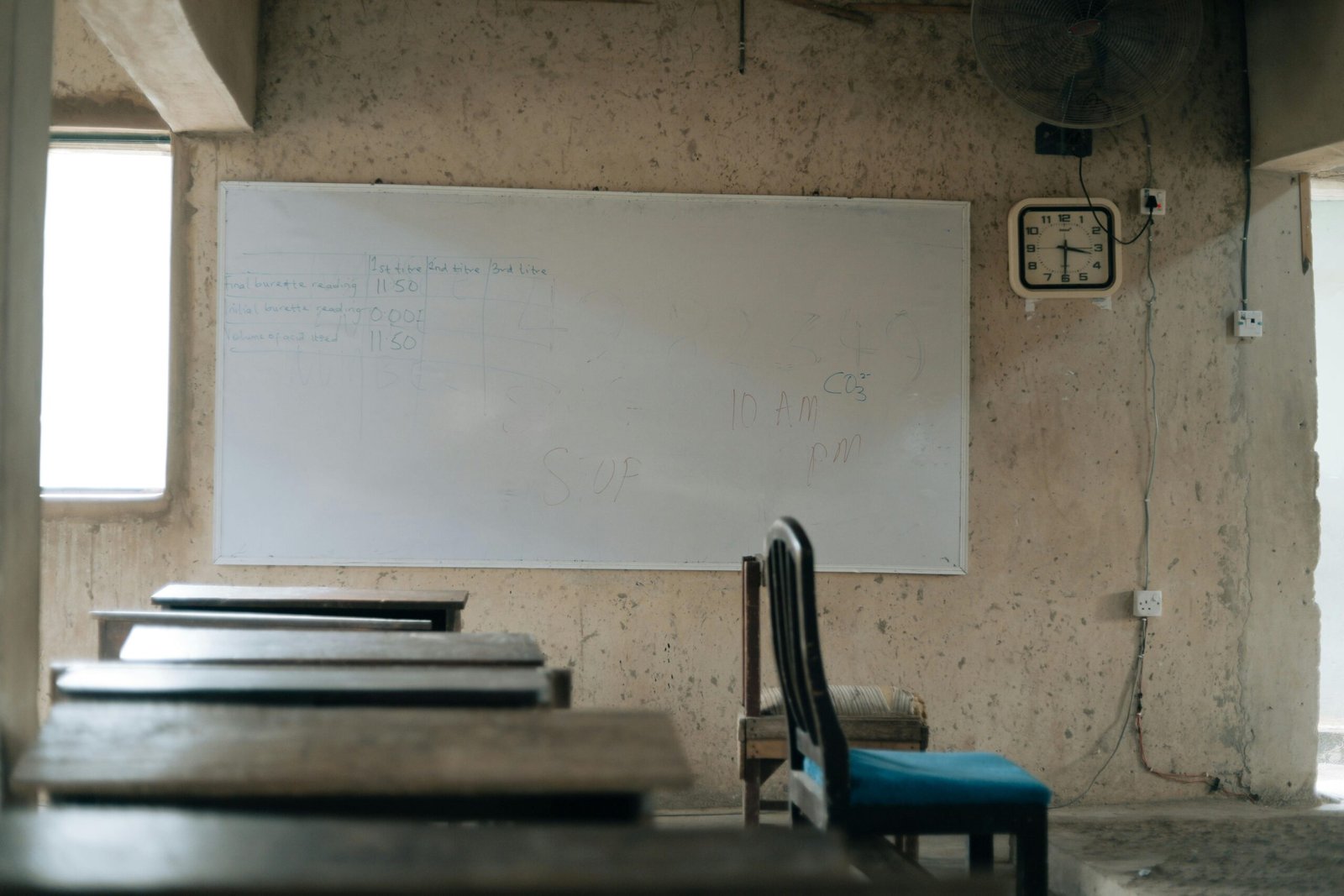 An empty classroom featuring old wooden desks, a whiteboard, and a wall clock, highlighting education.
